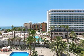 Un hotel con zona de piscina, palmeras y vista al océano.