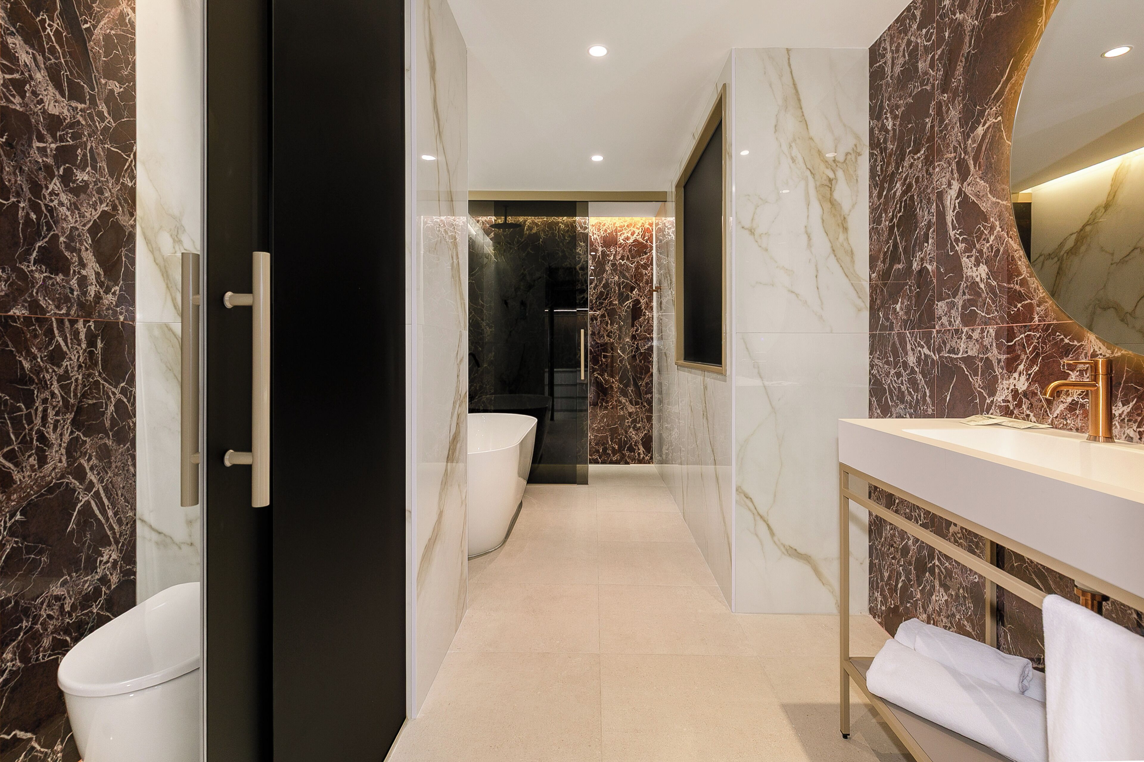 Une salle de bain moderne avec un mur en marbre, une baignoire et un meuble-lavabo doté d’un porte-serviettes.