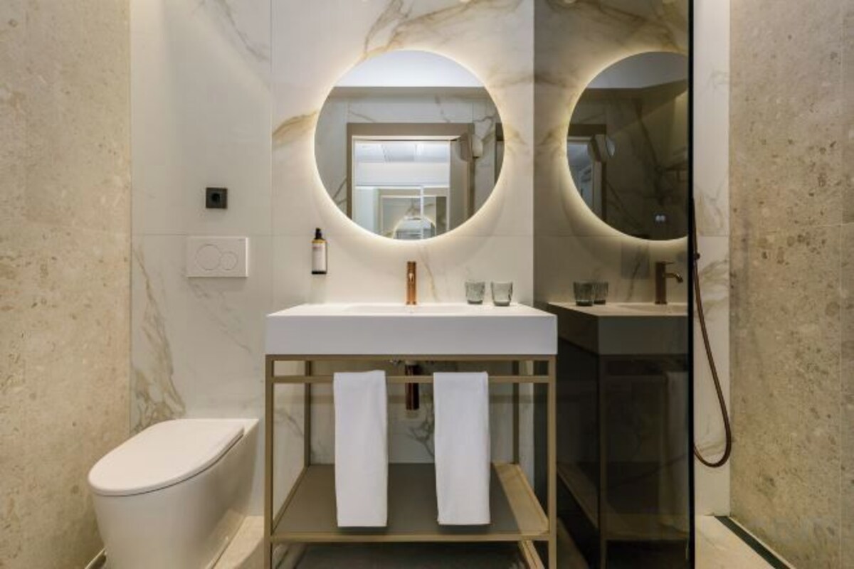 A modern bathroom with a marble wall, a round mirror above the sink, and a glass shower enclosure.