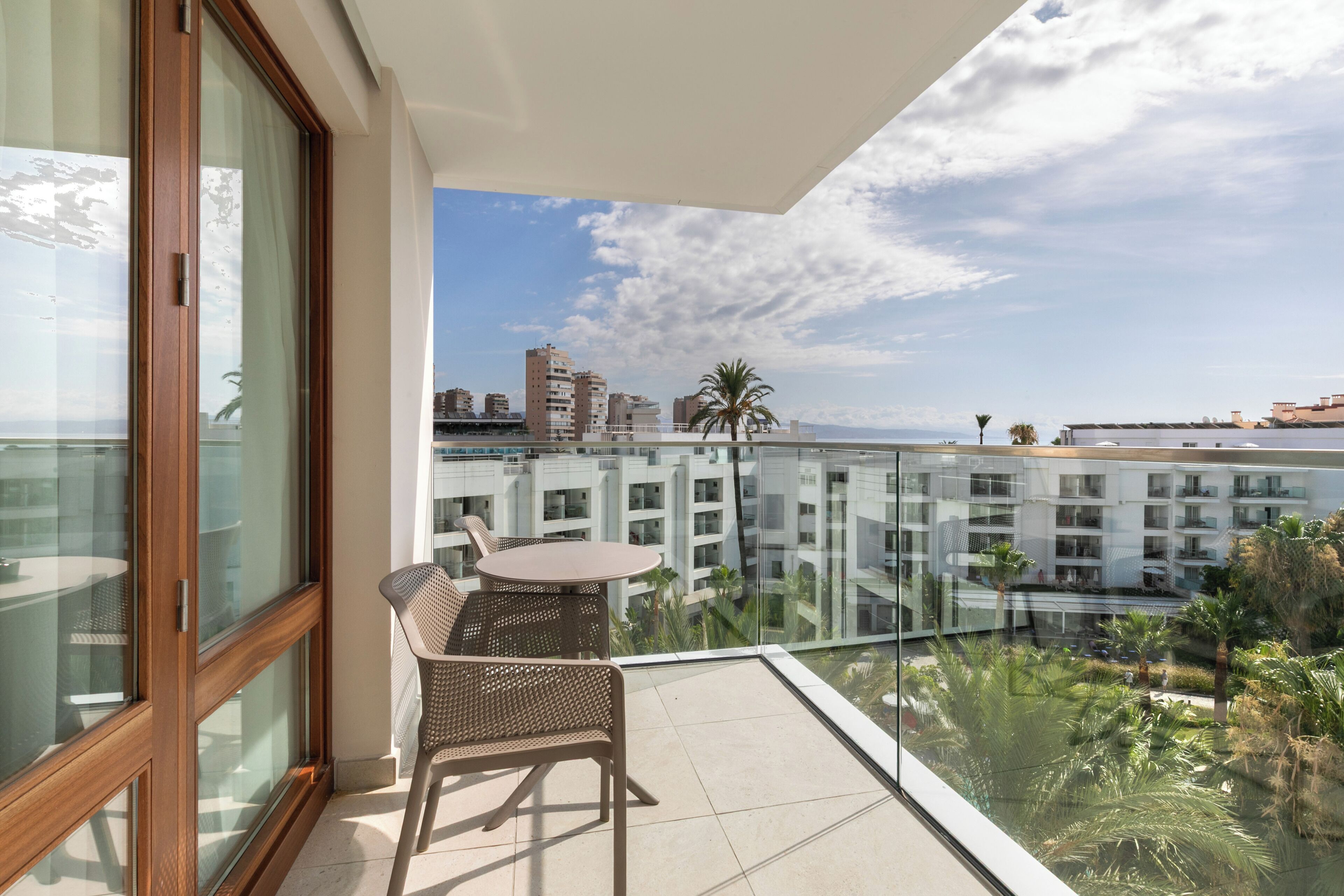 Un balcón con una mesa y sillas, con vista a un paisaje urbano con edificios y palmeras.