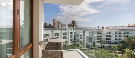 Un balcón con una mesa y sillas, con vista a un paisaje urbano con edificios y palmeras.