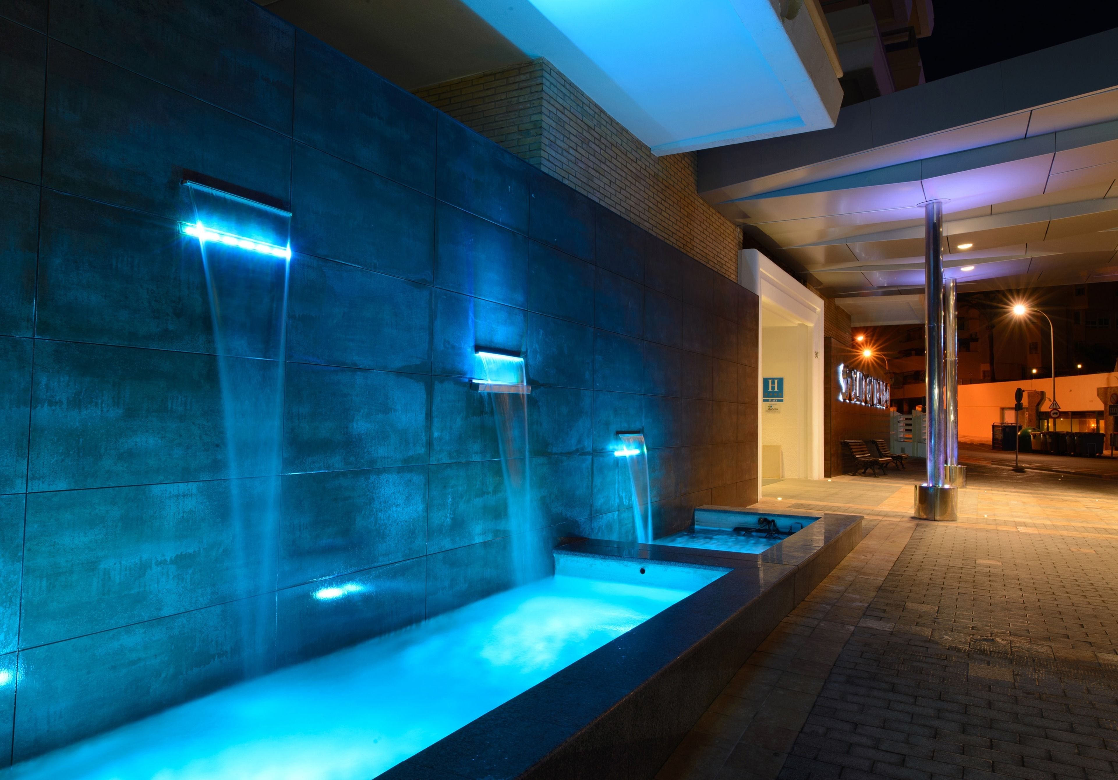 Een wellnessruimte met een groot bad en twee kleinere baden, verlicht met blauw licht.