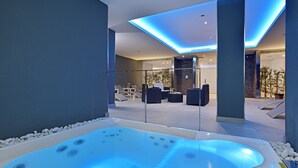 Un moderno espacio de spa con una bañera de hidromasaje, sillones reclinables y una zona de estar con paredes de cristal.