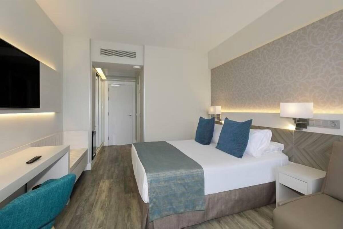 Een hotelkamer met een bed, nachtkastjes, een televisie en een badkamer die door een geopende deur zichtbaar is.