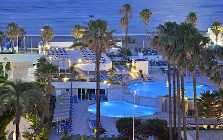 A resort with multiple pools, sun loungers, and palm trees.