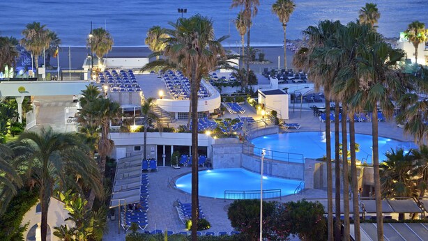 Un resort con varias piscinas, tumbonas y palmeras.