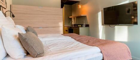A hotel room with a bed, a TV mounted on the wall, and a kitchenette area.