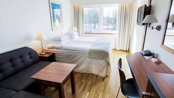 Ett hotellrum med en säng, en soffa, ett skrivbord, en stol, en lampa, en telefon och en tavla på väggen.