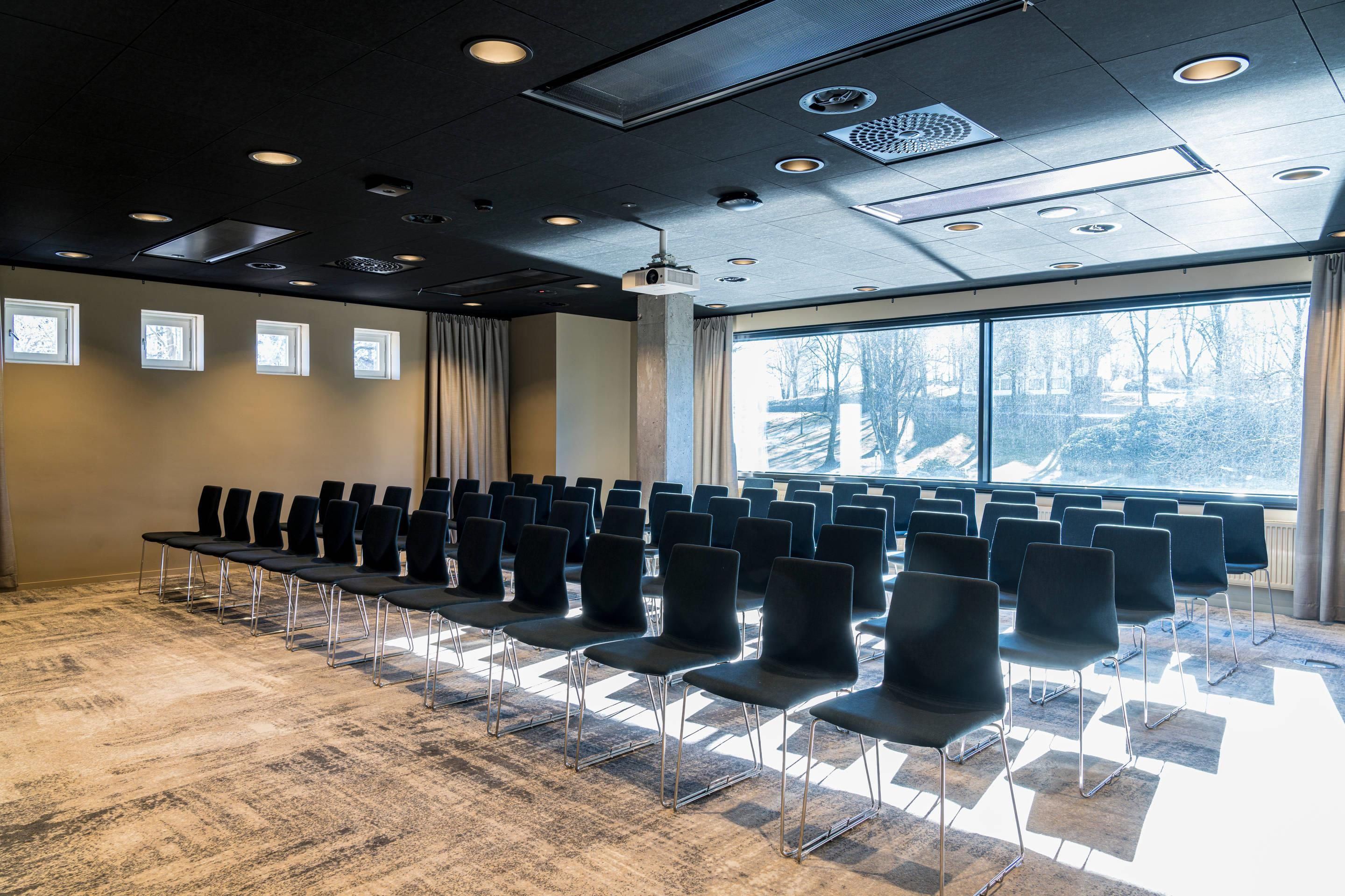 A conference room with rows of chairs, a projector, and a large window with a view of trees.