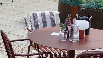 An outdoor seating area with round tables and metal chairs, surrounded by potted plants and a large planter.