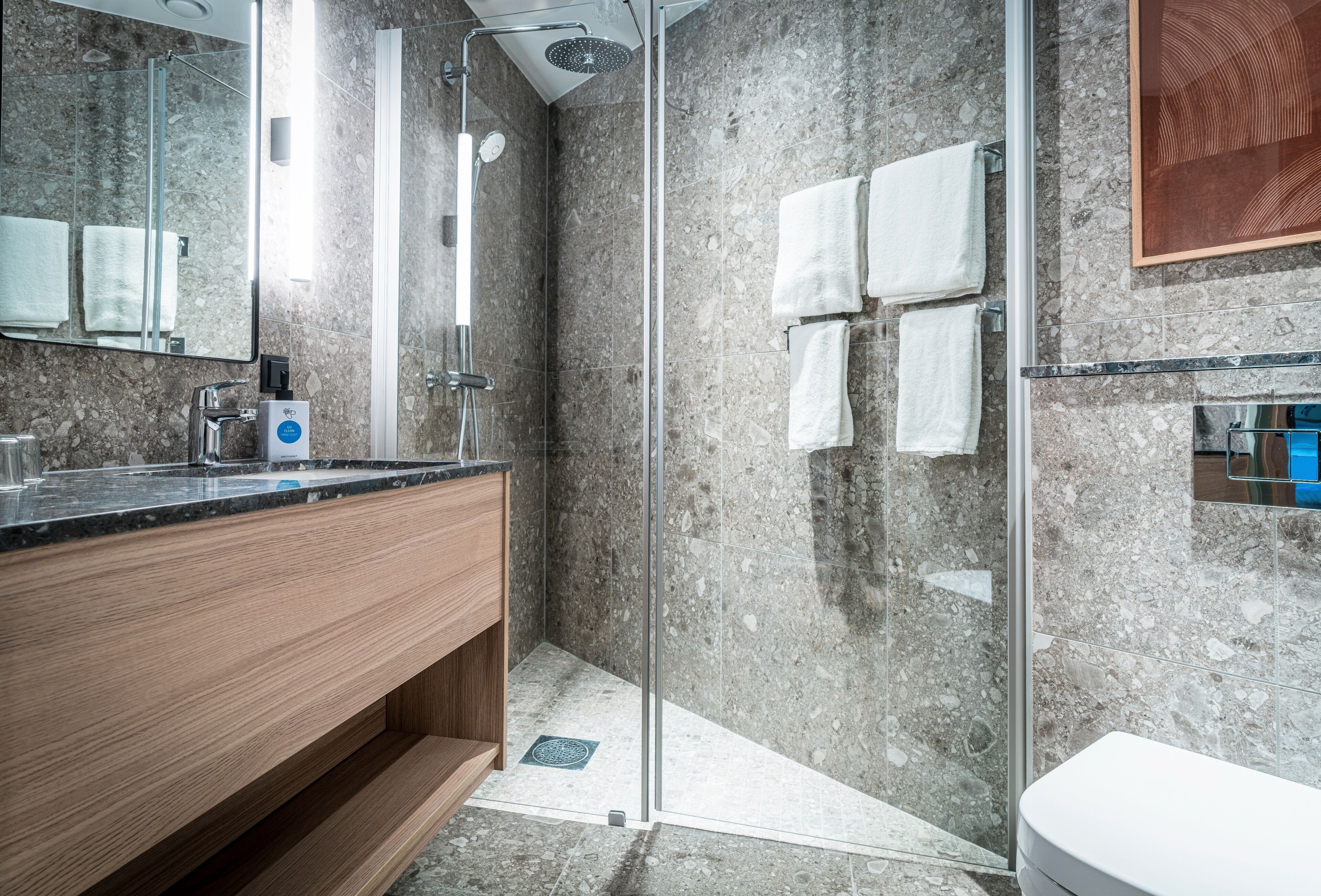 A modern bathroom with a glass-enclosed shower, a wooden vanity, and a marble backsplash.