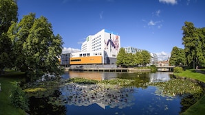 A modern building with a large mural, surrounded by a pond with lily pads and a grassy area. - Quality Hotel Grand Boras (Borås)