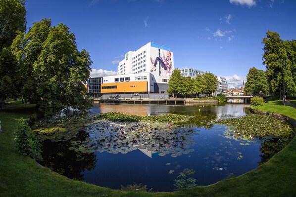 Un edificio moderno con un gran mural, rodeado por un estanque con nenúfares y un área verde.
