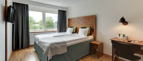 Una habitación de hotel moderna con una cama grande, un escritorio y un televisor montado en la pared.