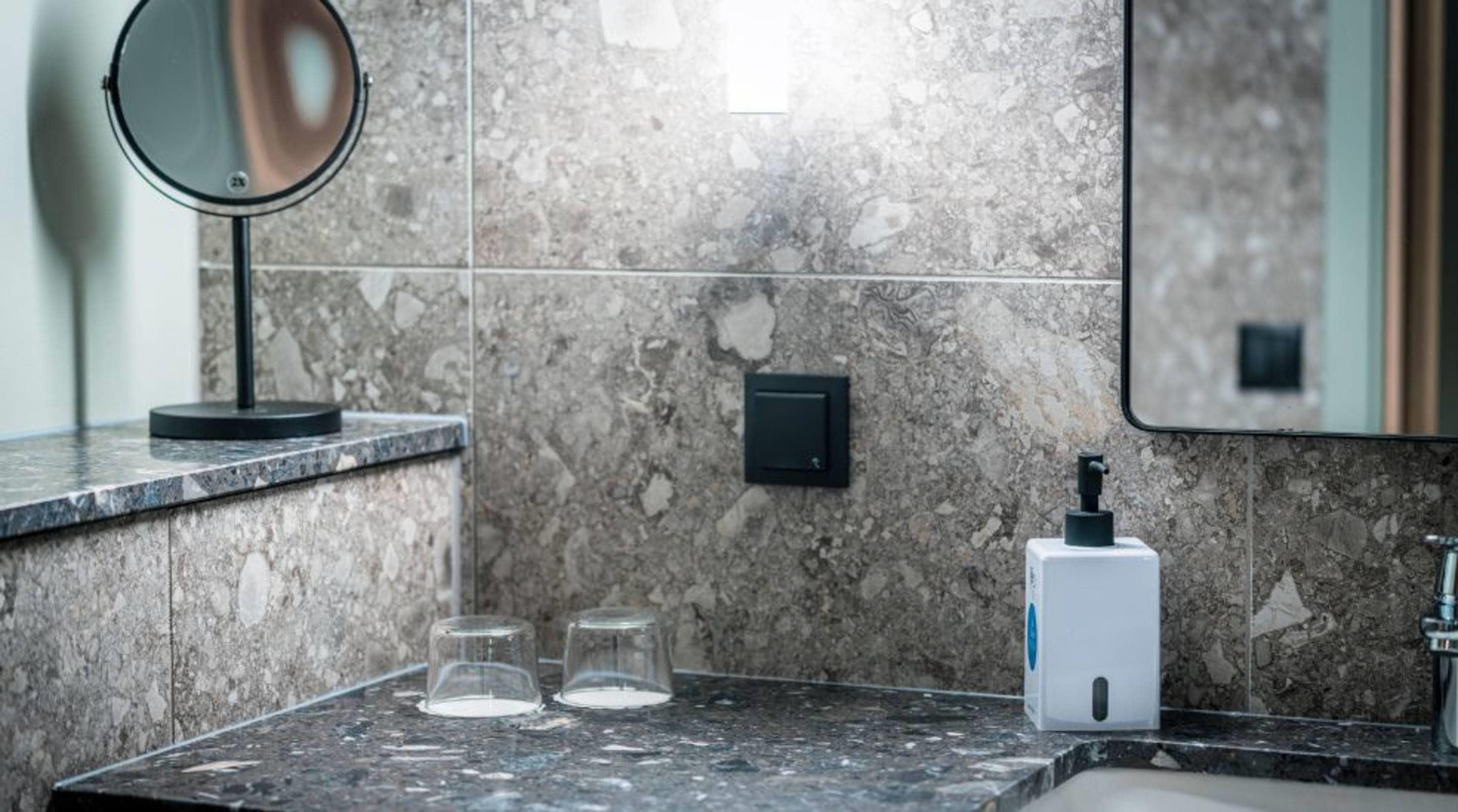 Un bagno con una parete in marmo, uno specchio, un dispenser di sapone e due bicchieri sul lavabo.