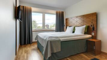 Un hotel moderno con una cama grande, un cabecero de madera, una mesita de noche y vistas al exterior.