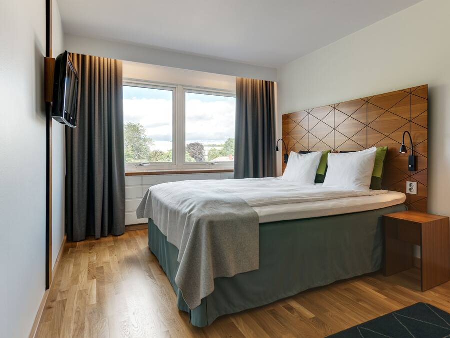 Un hotel moderno con una cama grande, un cabecero de madera, una mesita de noche y vistas al exterior.