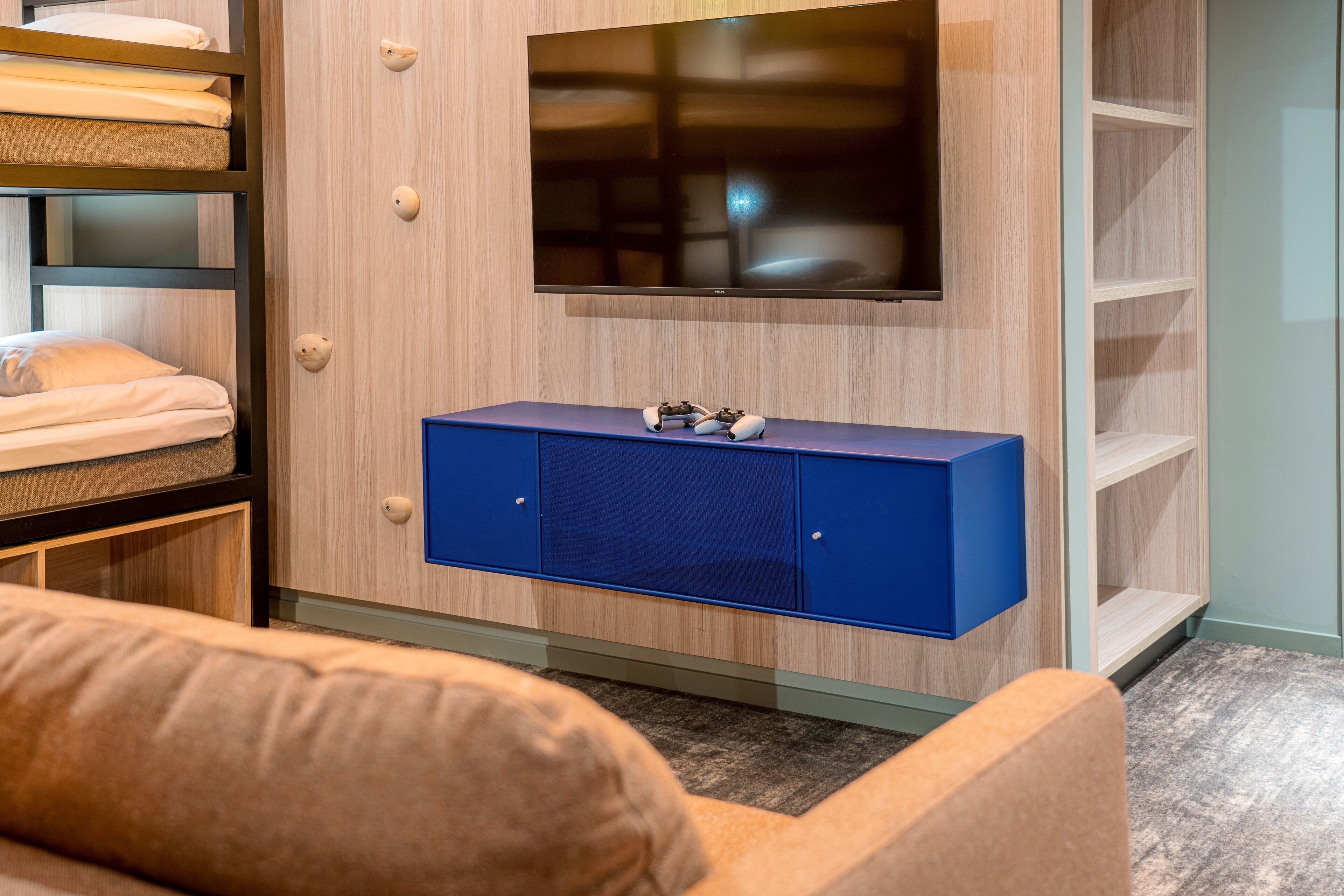 Una habitación moderna con televisor montado, un armario azul y estanterías empotradas.