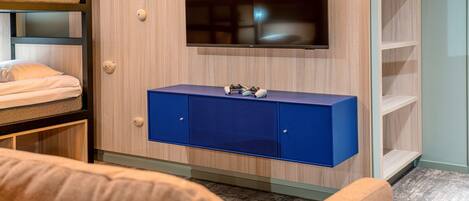 Una habitación moderna con televisor montado, un armario azul y estanterías empotradas.