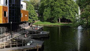 A modern building with a glass facade, a dock extending into a calm lake, and a waterfall in the background.