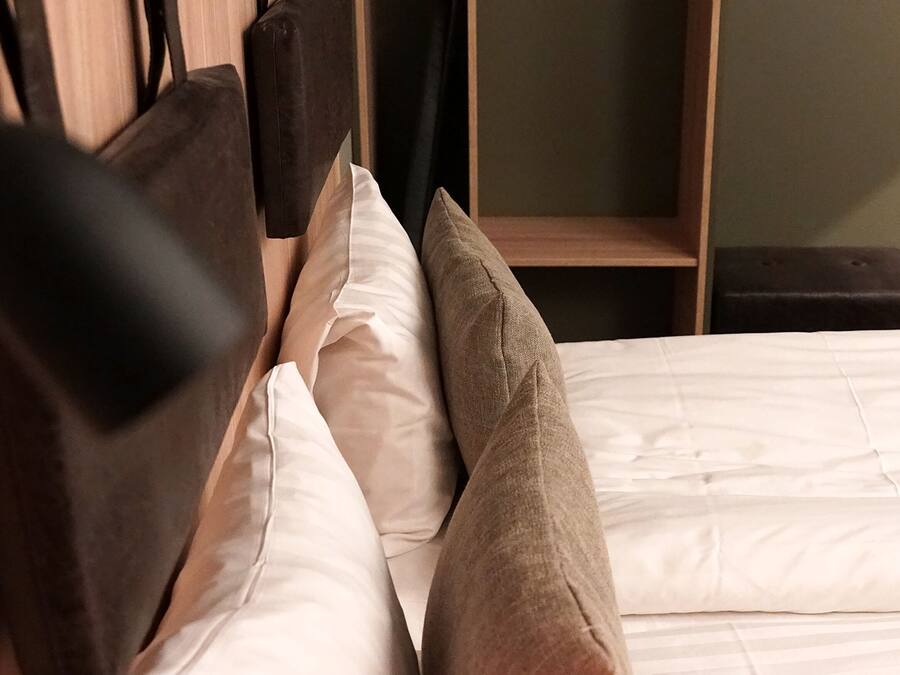 A bed with a wooden headboard, white bedding, and two pillows.