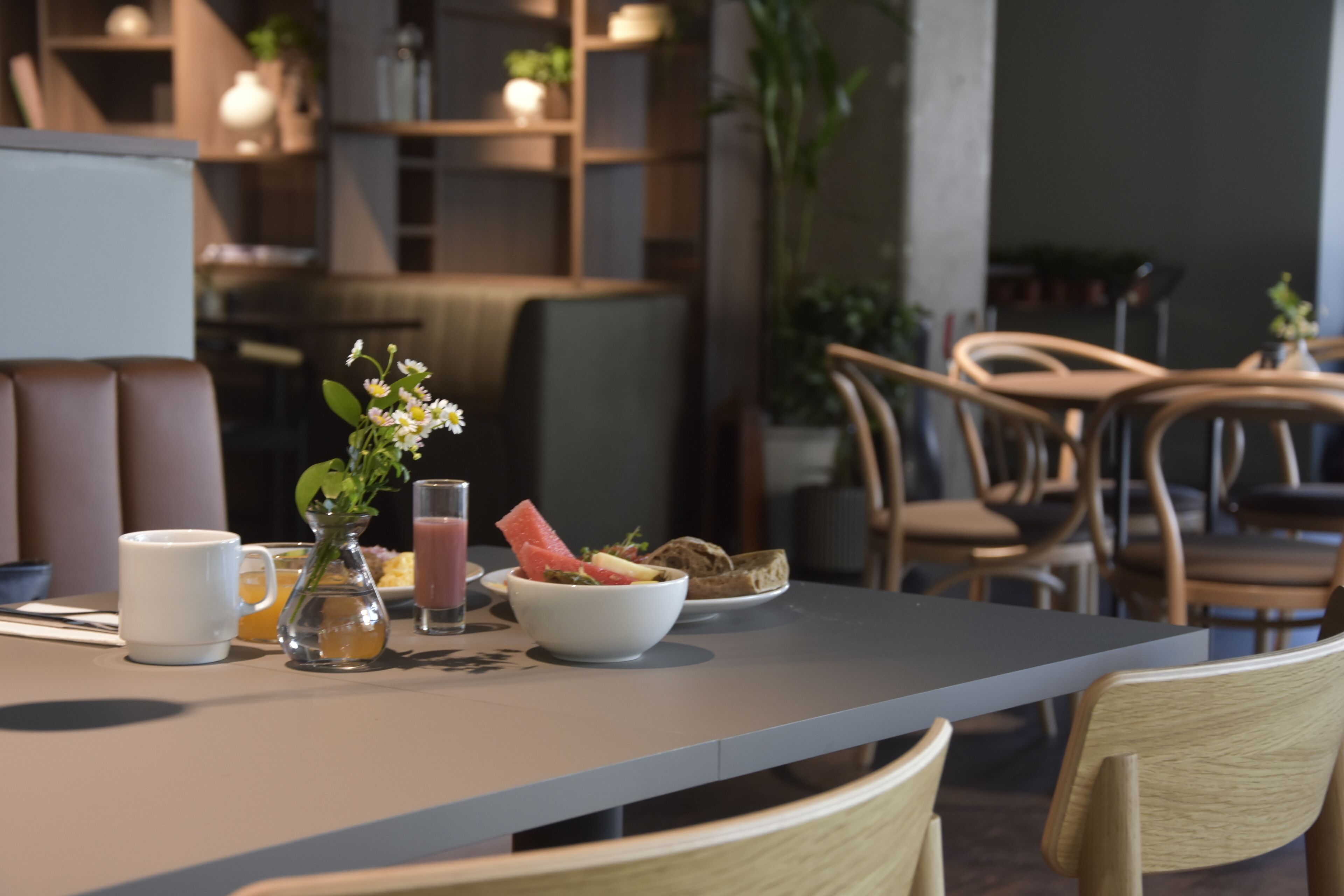 A dining area with a table set for breakfast, including a bowl of fruit, a glass of juice, and a white mug.