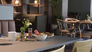 A dining area with a table set for breakfast, including a bowl of fruit, a glass of juice, and a white mug.