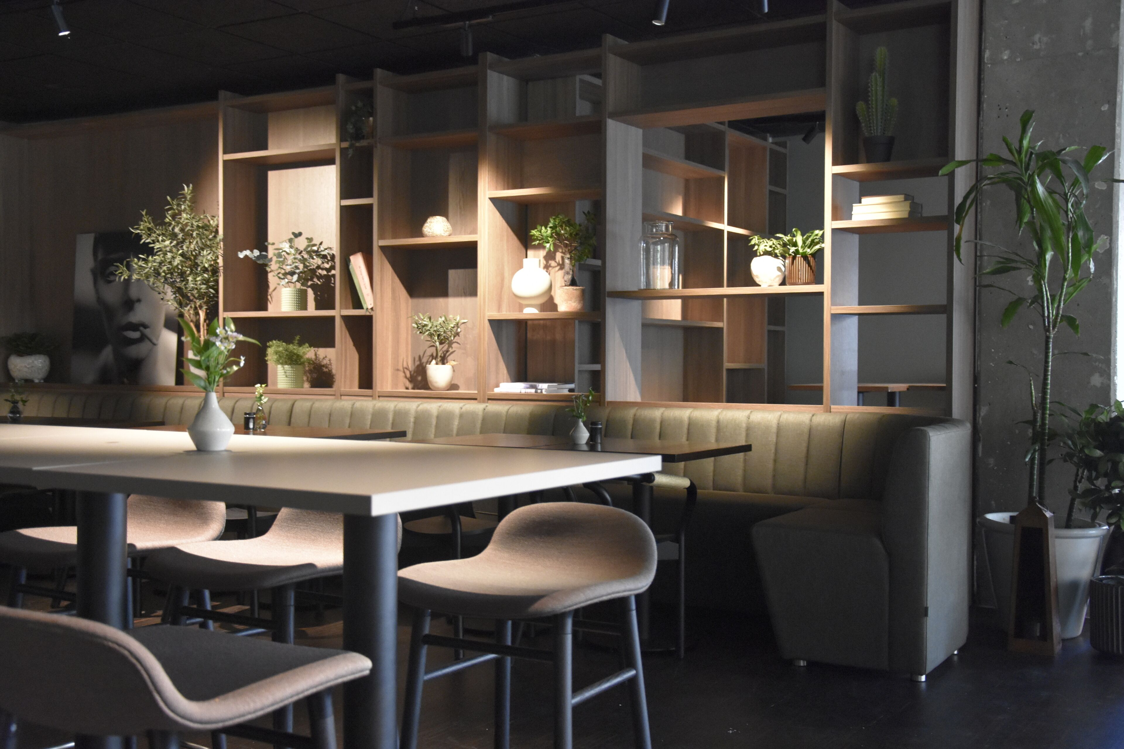 Um restaurante moderno com uma mesa comunitária grande, assentos acolchoados e prateleiras de madeira com plantas.