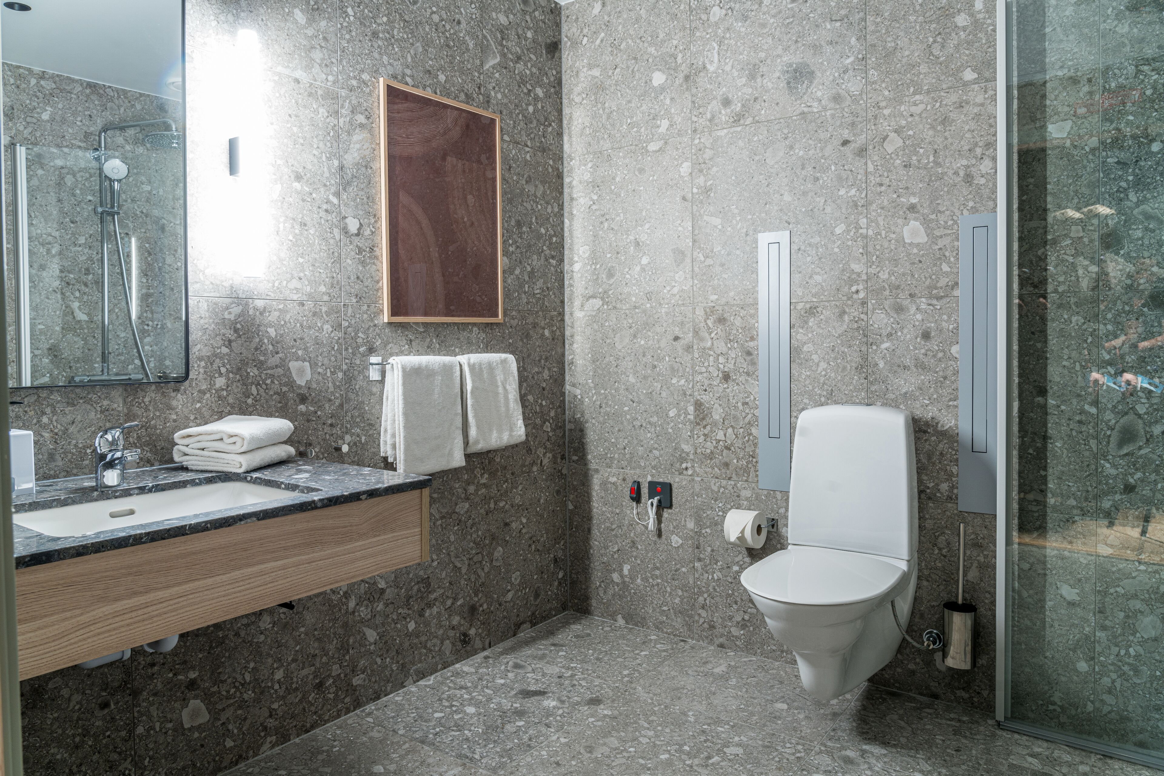 Ein modernes Badezimmer mit Granitwaschtisch, Holzschrank, großem Spiegel, Toilette und einer Duschkabine.