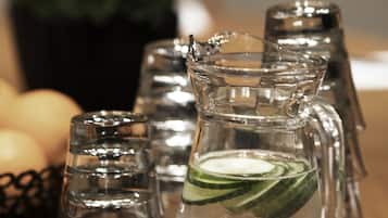 A clear glass pitcher with a mint leaf, surrounded by empty glass cups on a wooden table.