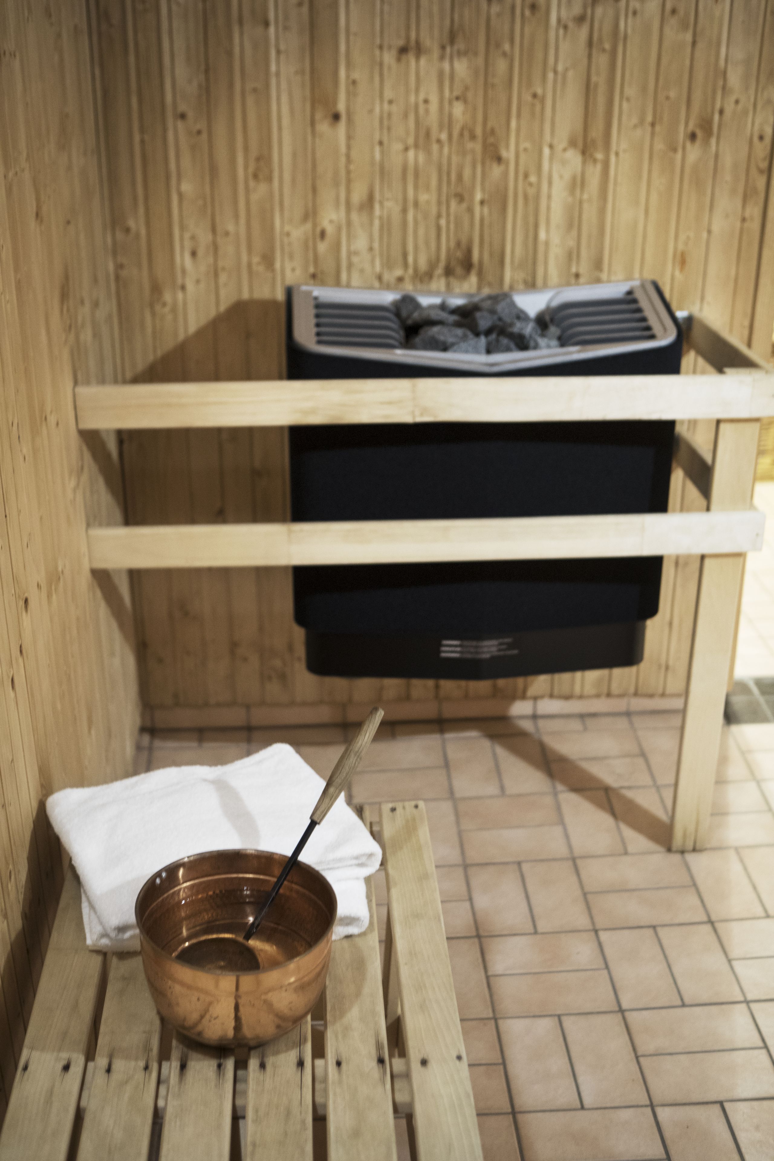 Un banc en bois pour sauna, avec un récipient en cuivre et une serviette.
