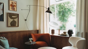 Un salon moderne comprenant un canapé, un fauteuil, une table ronde et une grande fenêtre donnant sur un paysage verdoyant.