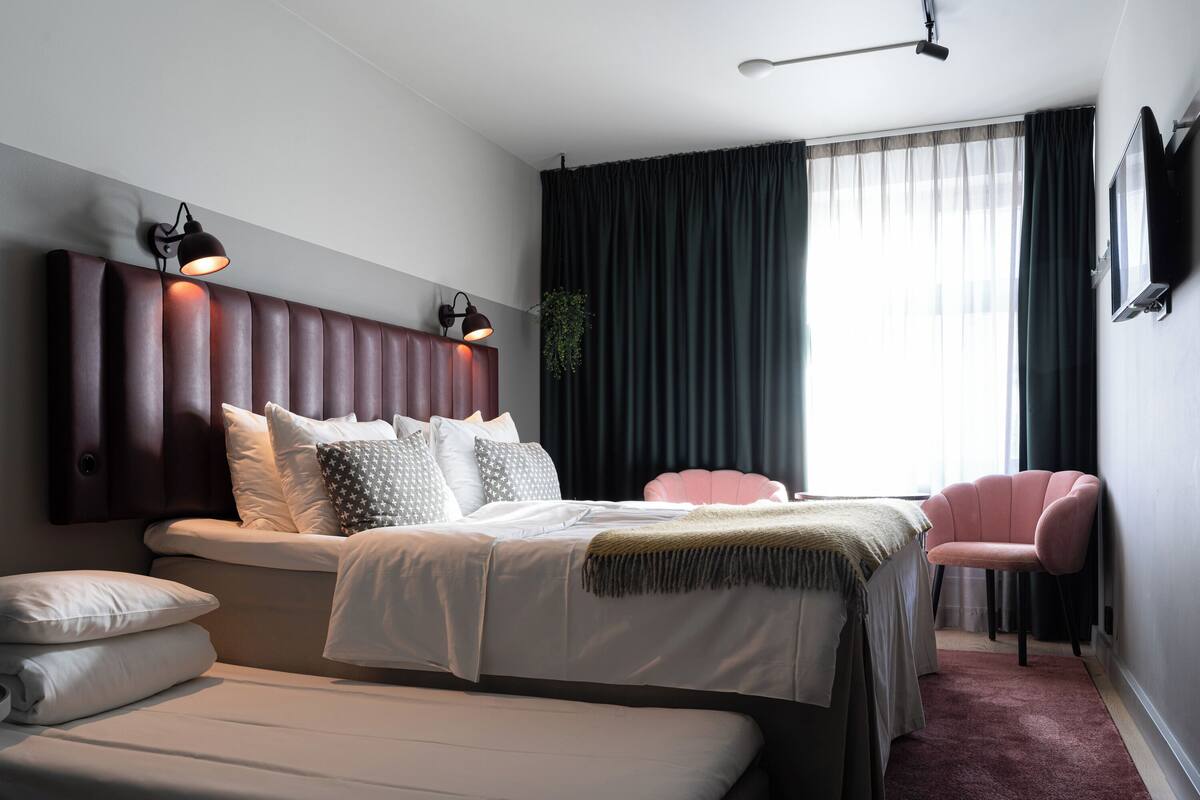 Ein modernes Hotelzimmer mit einem großen Bett, einem Einzelbett, einem rosa Sessel und einem Fernseher an der Wand.
