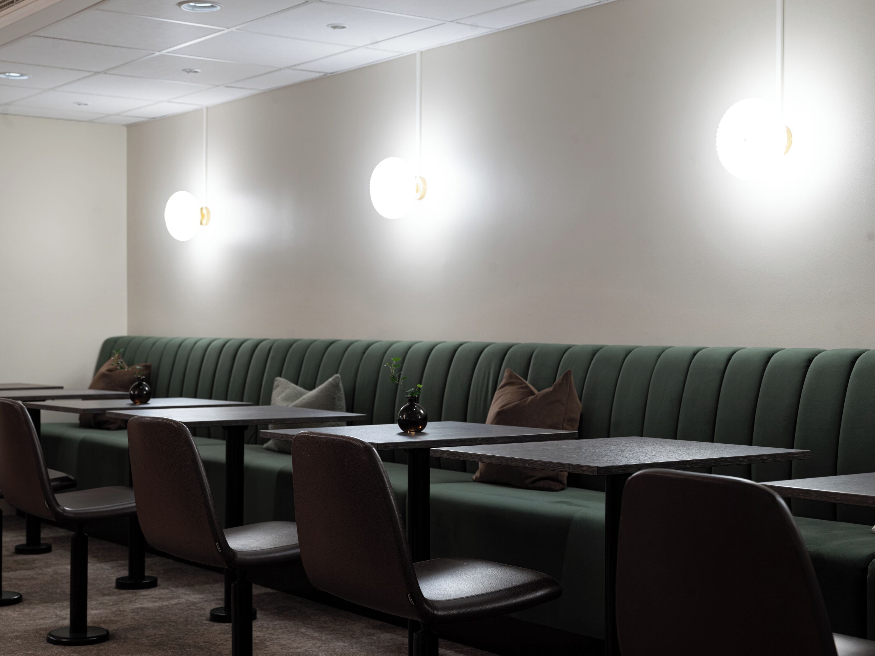 A restaurant interior with green upholstered booths, black chairs, and tables.