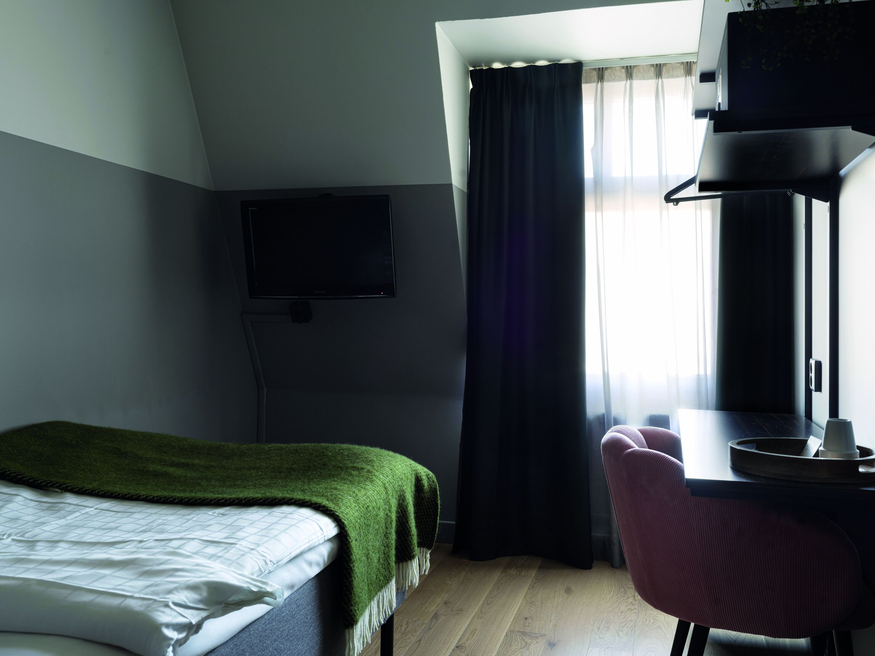 A hotel room with a bed, a desk, a chair, a TV, and a window with curtains.