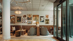 Un hall d’entrée moderne agrémenté d’un grand tapis à motifs, d’un espace salon avec des fauteuils à rayures et de diverses œuvres d’art encadrées qui ornent les murs.