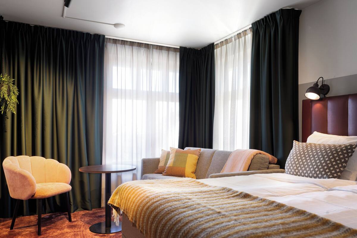 Ein Hotelzimmer mit einem Bett, einer Couch, einem Sessel, einem kleinen Tisch und einer Lampe.