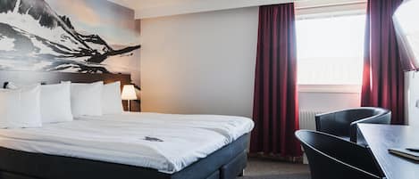 A hotel room with a bed, a desk, a chair, a lamp, and a large window with curtains.