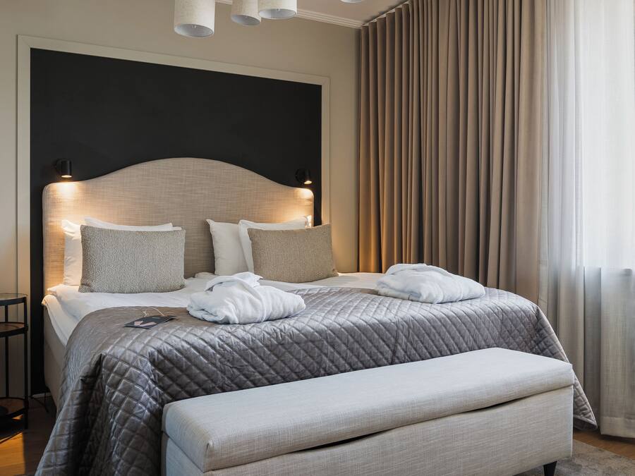 Una habitación de hotel moderna con una cama grande, una mesita de noche y vistas a la ciudad a través de la ventana.