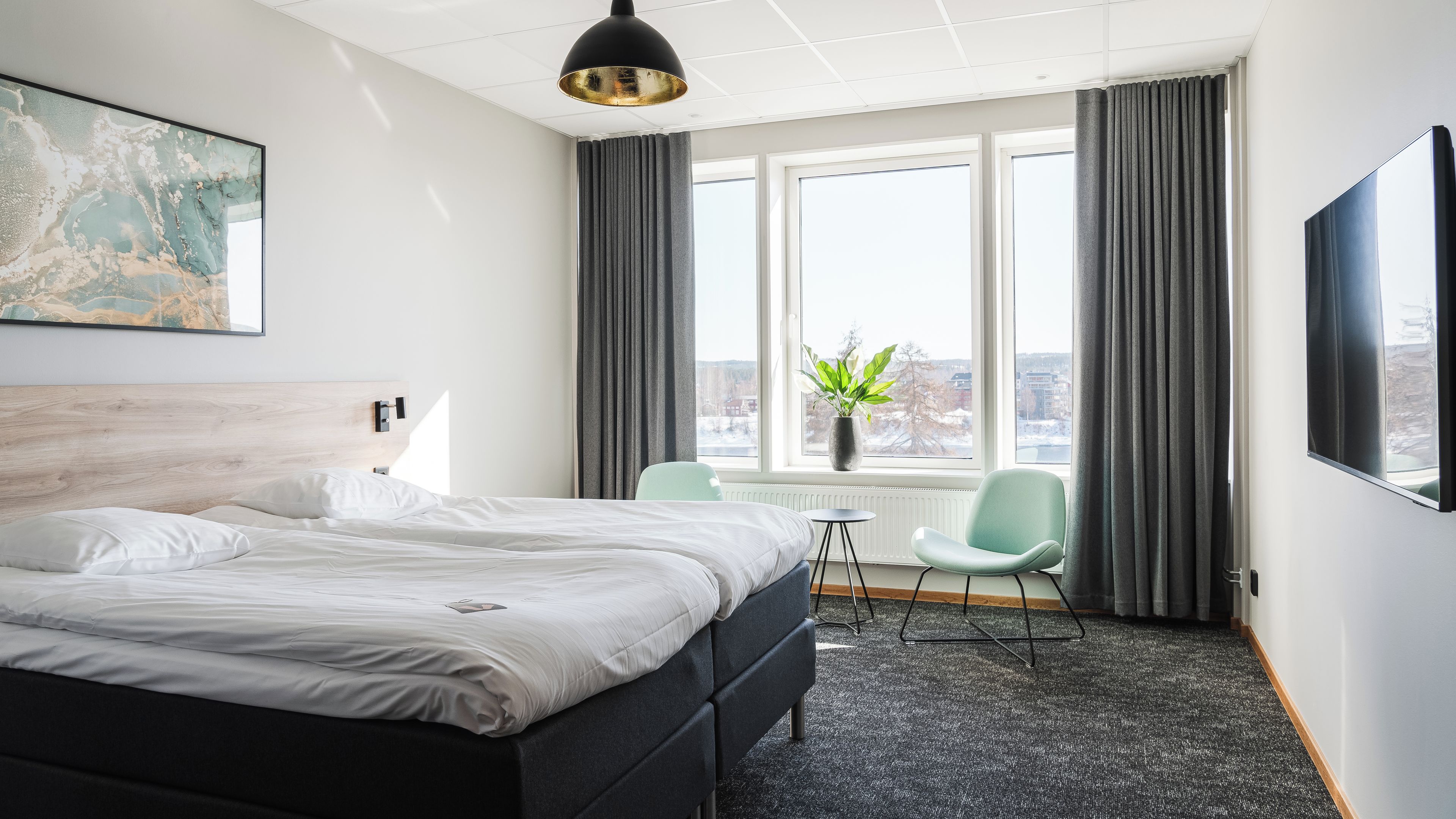 A hotel room with a bed, a chair, a table, a large window, and a painting on the wall.