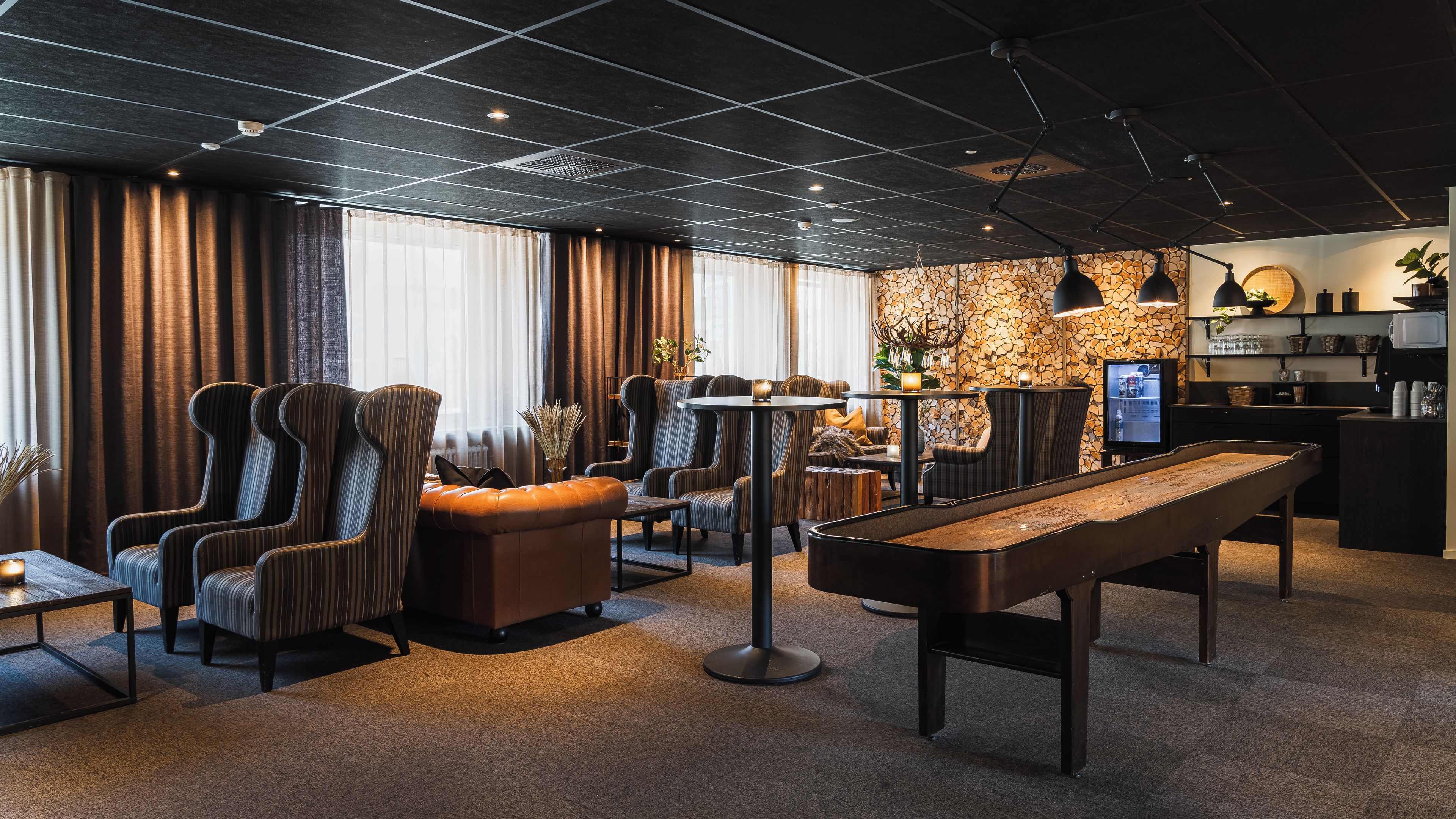 Un espace de détente moderne avec des fauteuils à rayures, une table de billard et un mur en pierre en arrière-plan.
