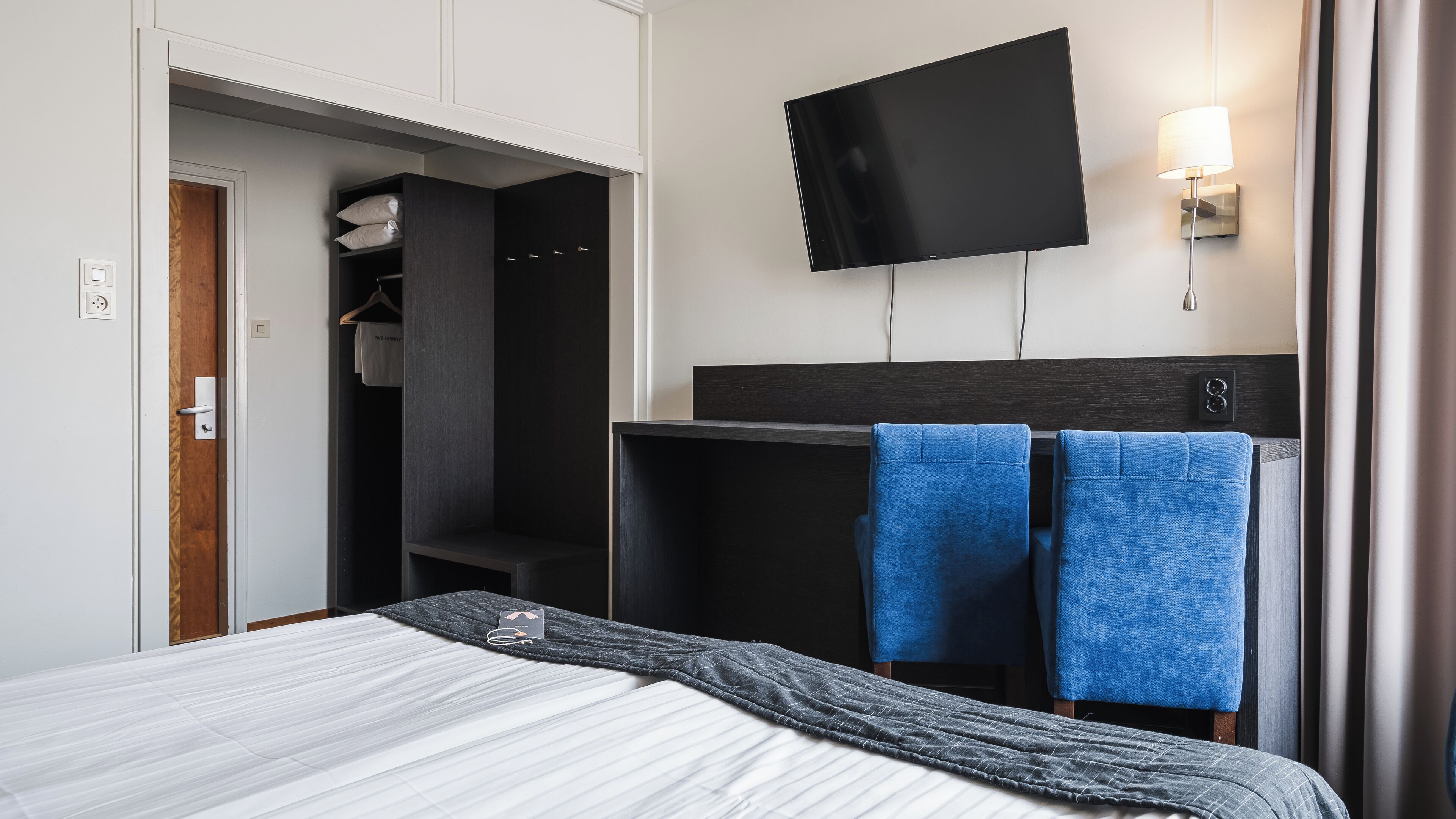 Ett hotellrum med en säng, en tv som är monterad på väggen, en garderob och ett badrum som syns genom en öppen dörr.