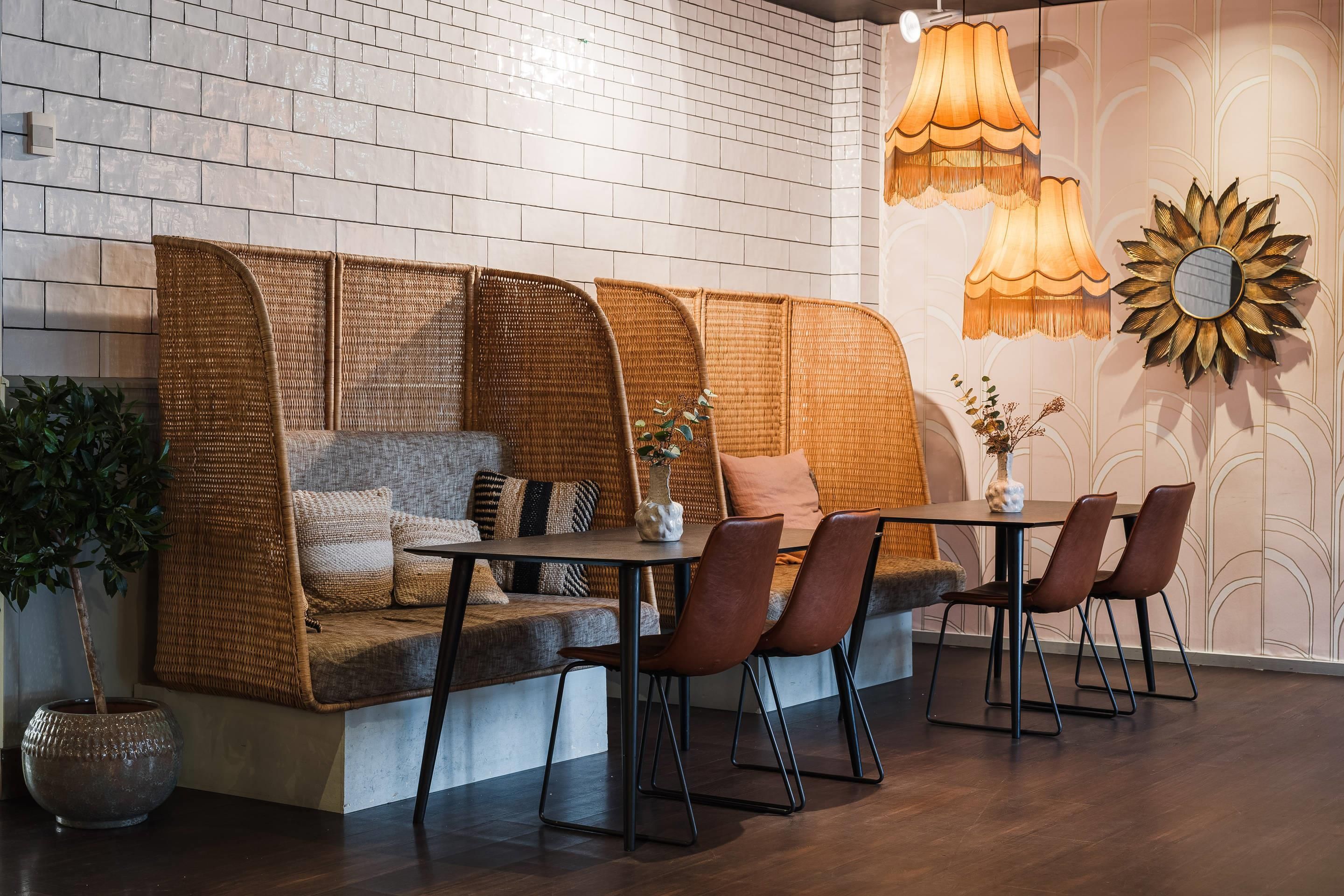 A cozy seating area with a woven sofa, a dining table, and chairs, accompanied by a vase and a potted plant.