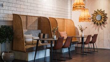 A cozy seating area with a woven sofa, a dining table, and chairs, accompanied by a vase and a potted plant.