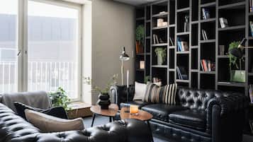 A modern living room with a leather sofa, a bookshelf, and a window with a view.