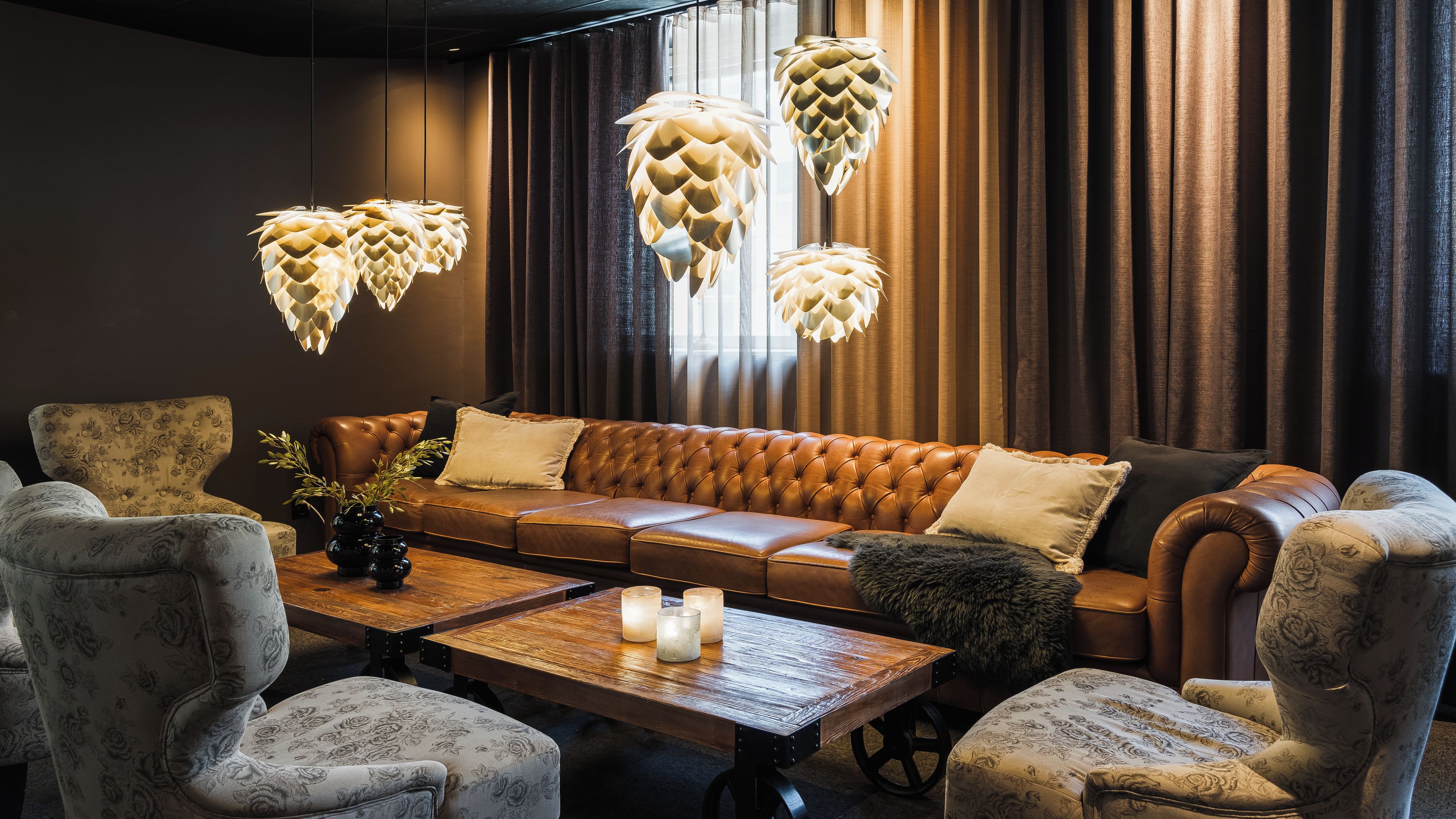 A modern living room with a leather sofa, patterned armchairs, a wooden coffee table, and decorative hanging lamps.