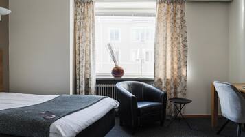 A hotel room with a bed, a desk, a chair, and a window with curtains.