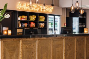 Een barruimte met een neonbord, schappen vol snacks, een koelkast met drankjes en hangende吊り下げ照明.