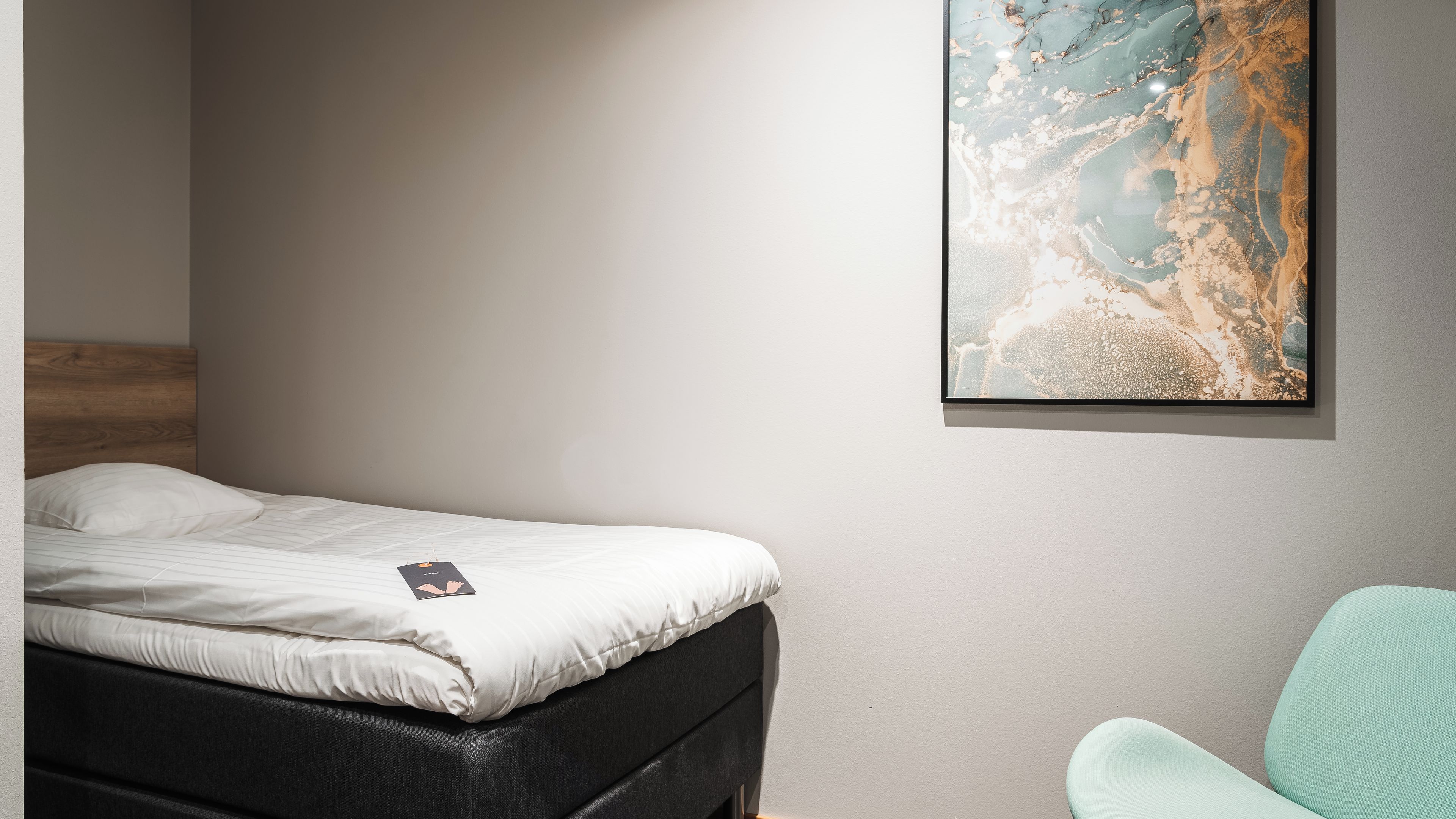 Un dormitorio con una cama, un cuadro abstracto colgado en la pared y una silla.