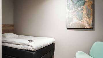 Un dormitorio con una cama, un cuadro abstracto colgado en la pared y una silla.